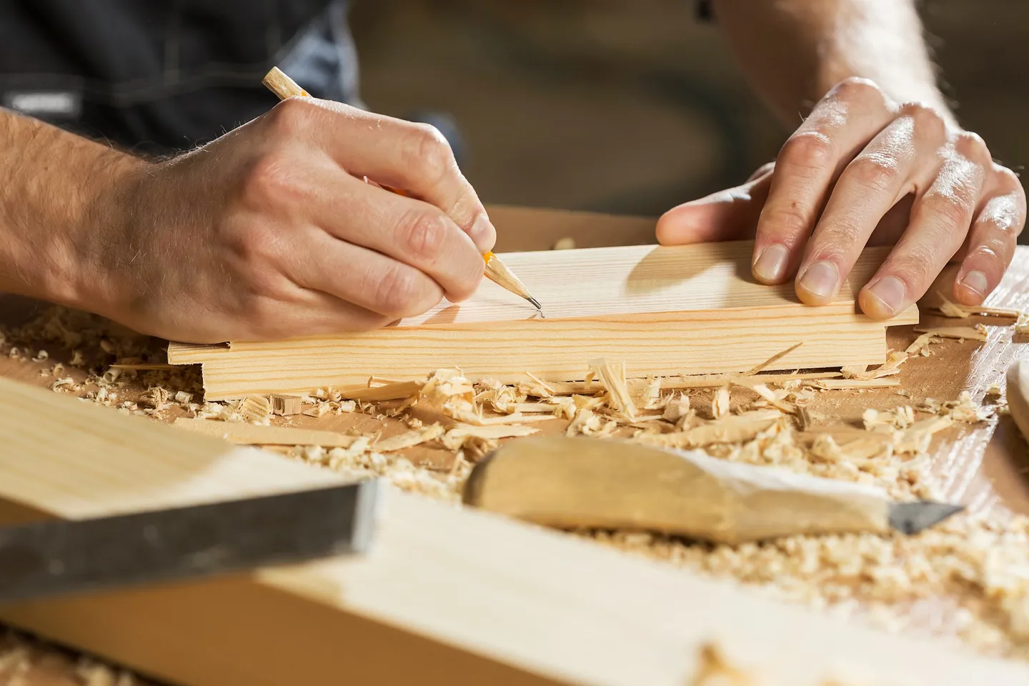 Hände zeichnen mit dem Bleistift eine Linie auf ein Holzstück, daneben Hobelspäne