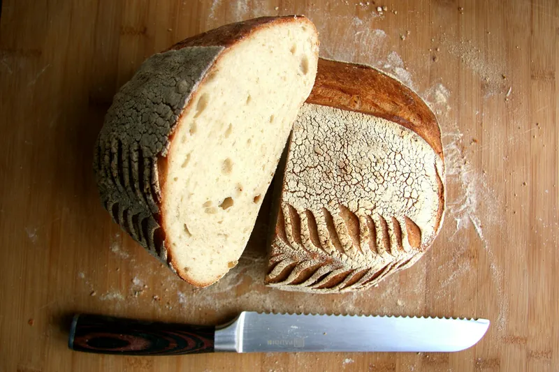 Angeschnittenes Sauerteigbrot auf einem Holzbrett, daneben ein Brotmesser