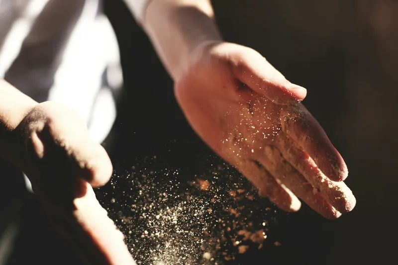 Eine Hand streut Mehl, die Körner stehen im Gegenlicht