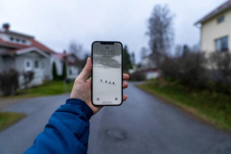 Eine Hand hält auf einer Straße in einem Wohngebiet ein Handy
